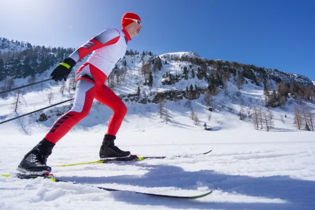 Cross-country skier in action, clear blue sky and sunshine, snowcapped mountains.