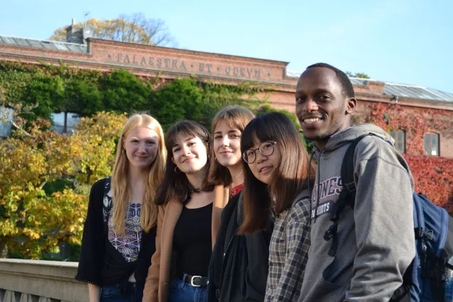 A group of international students posing in front of an autumnal Palaestra