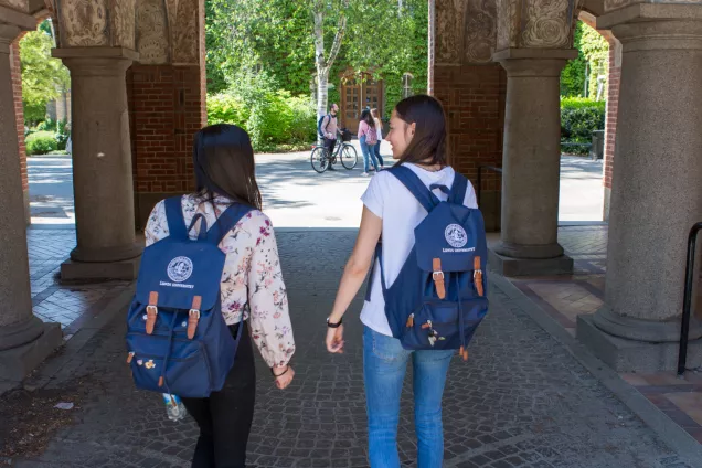 Two students walking through the gate separating the University Library and the Faculty of Social Sciences with LU backpacks
