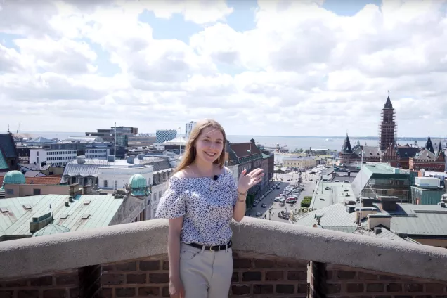 A student at Campus Helsingborg standing at a lookout point waving. Photo.