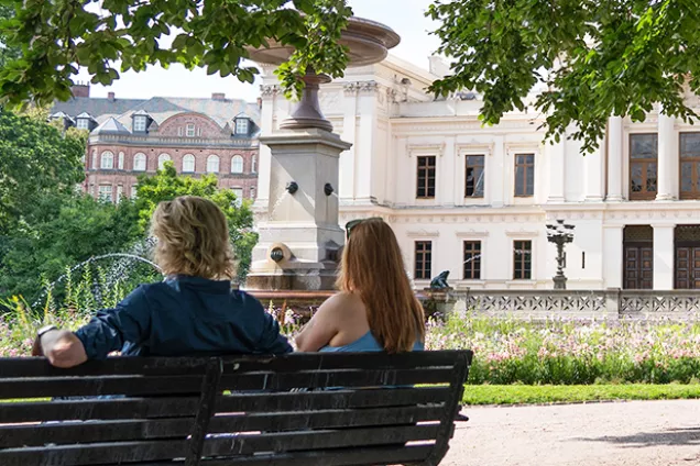 Two students sitting on a bench in front of the Main University Building.