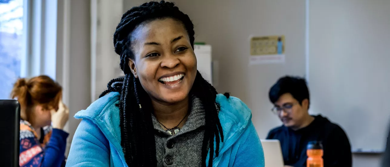 A smiling student at Graduate school with two other students in the background