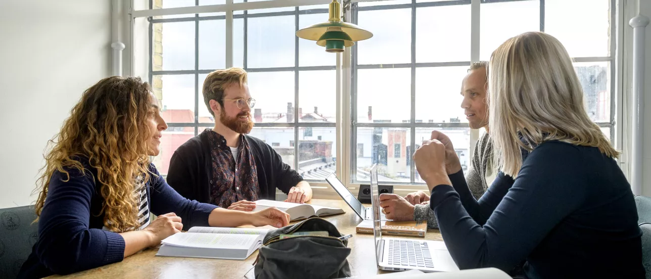 Four students discussing something in front of a large window at the Faculty of Law