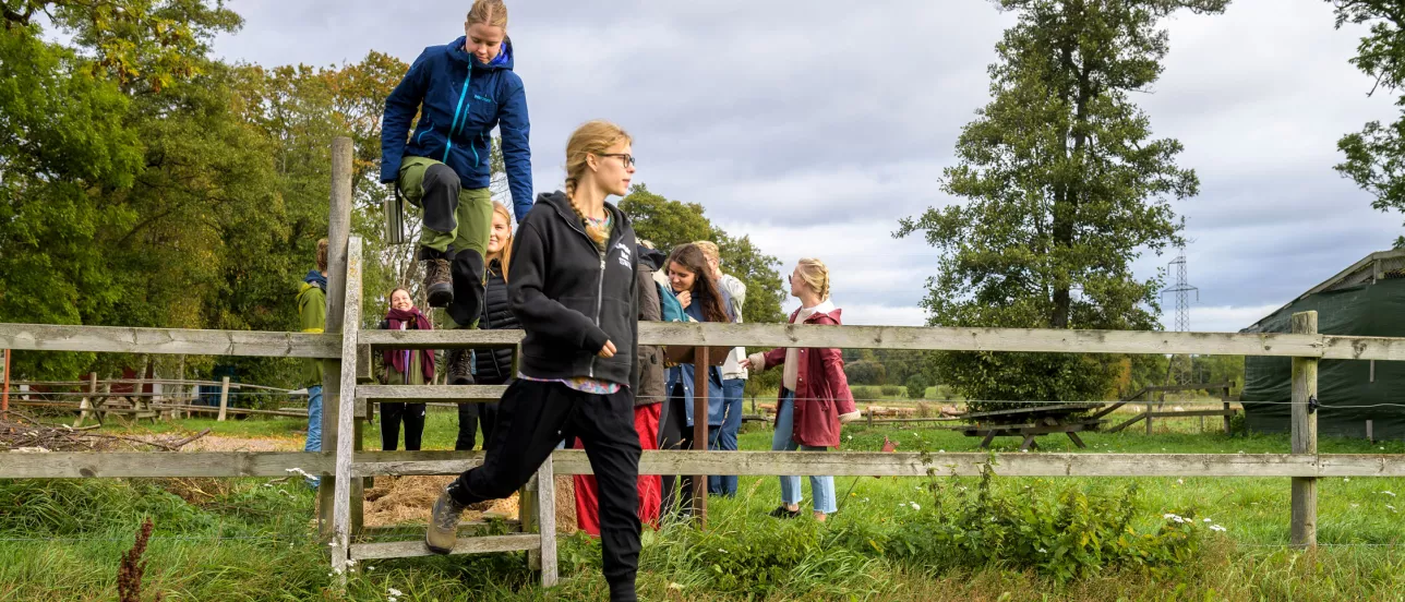 Students on an excursion climbing over a fence with both natural and cultural elements around them