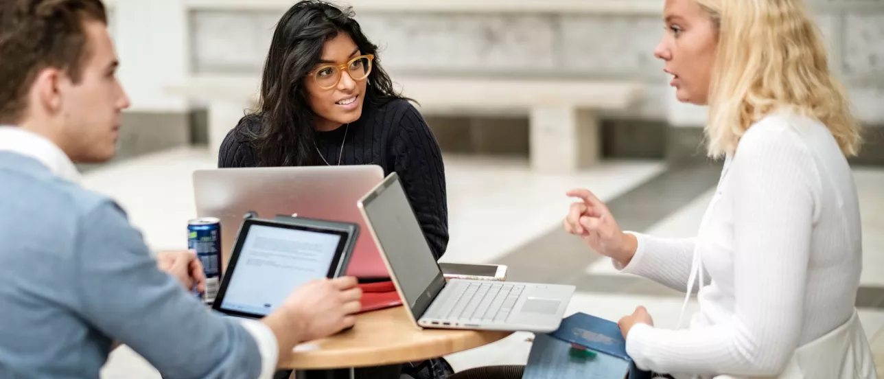 Three students with laptops discussing something