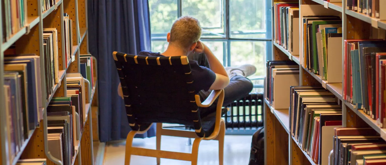 Someone in a comfortable chair reading a book at a library in front of a window