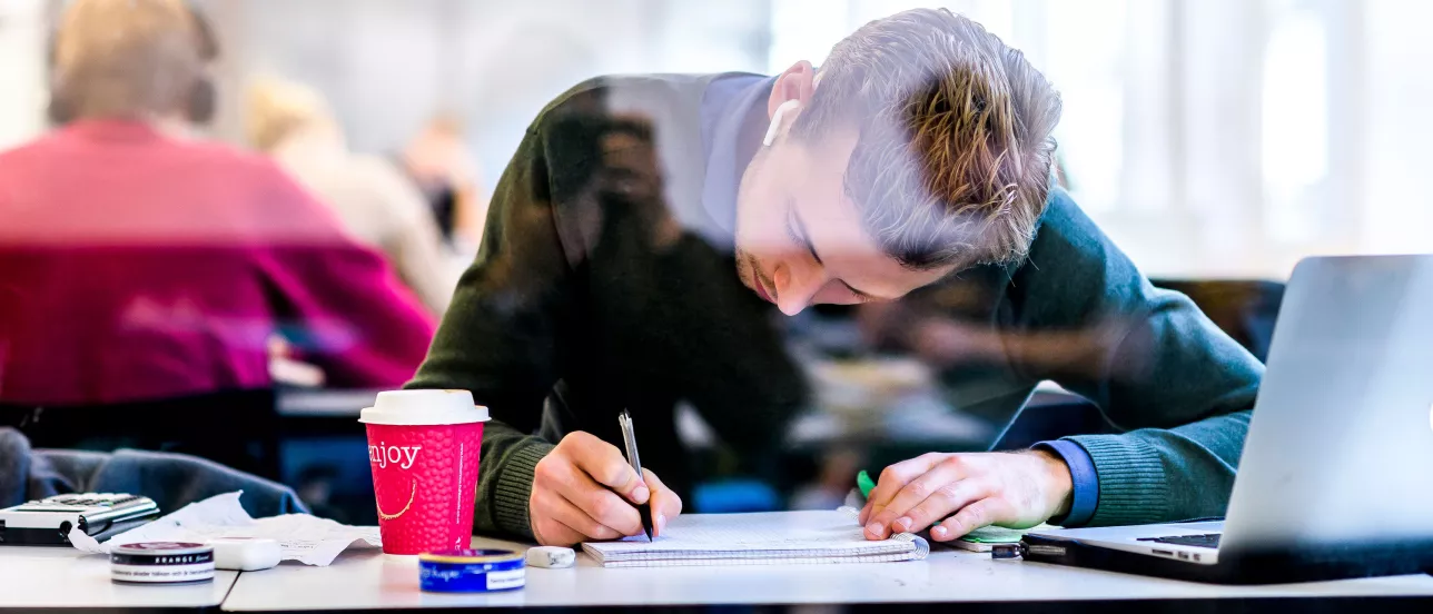 A student bending over their books and computer, a calculator lying next to him