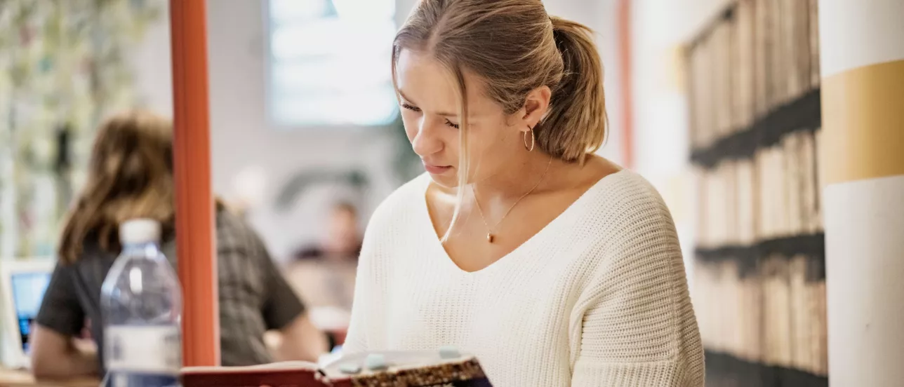 A student in a library reading in a thick book