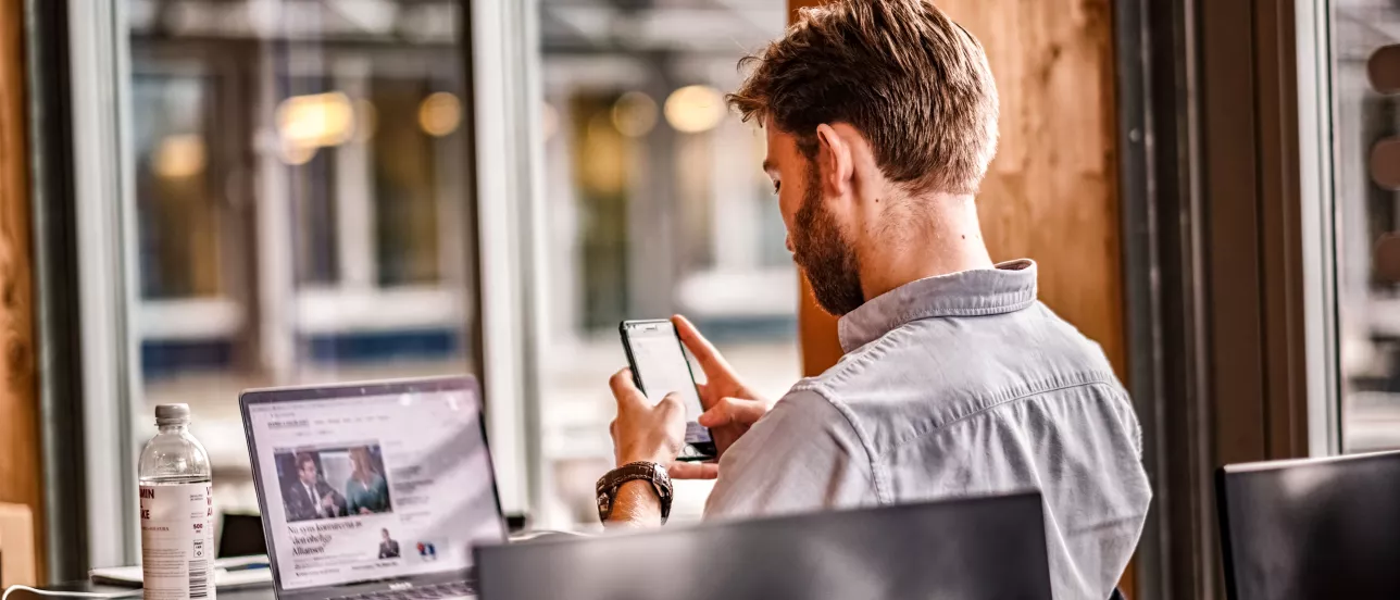 A student looking at a phone with a computer screen in the background