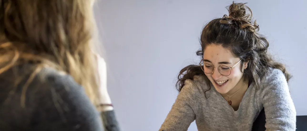 Two students working on an assignment together, writing and smiling