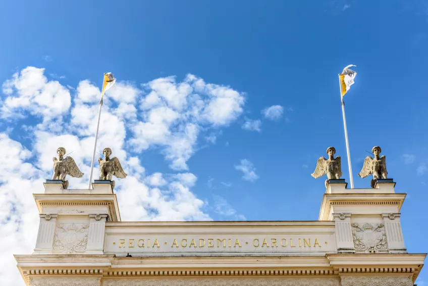 Part of the Main University Building's roof with statues and flags against a blue sky 