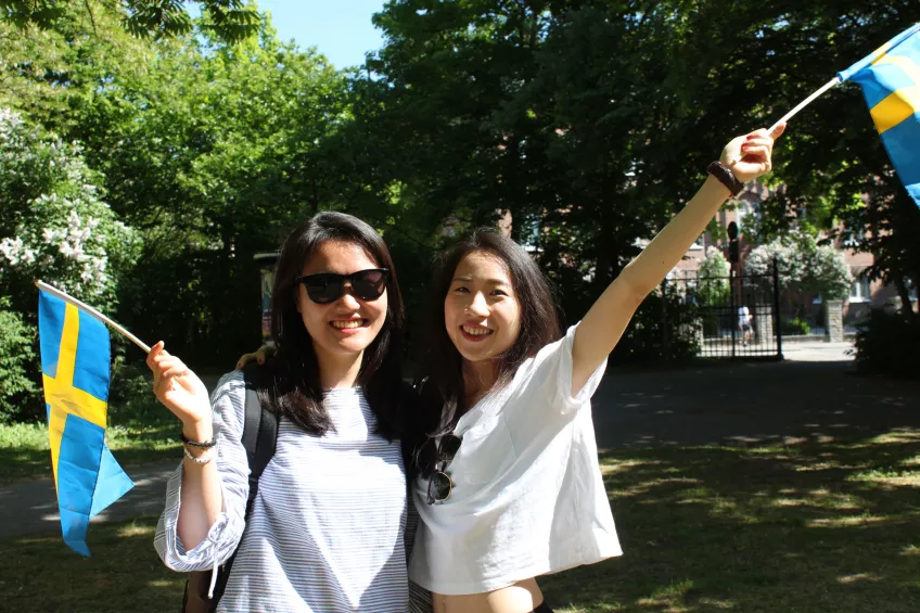 Two students waving Swedish flags outside