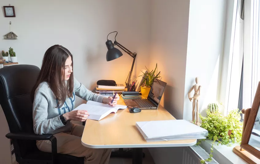 Student sitting by the desk in her student accommodation. Photo.