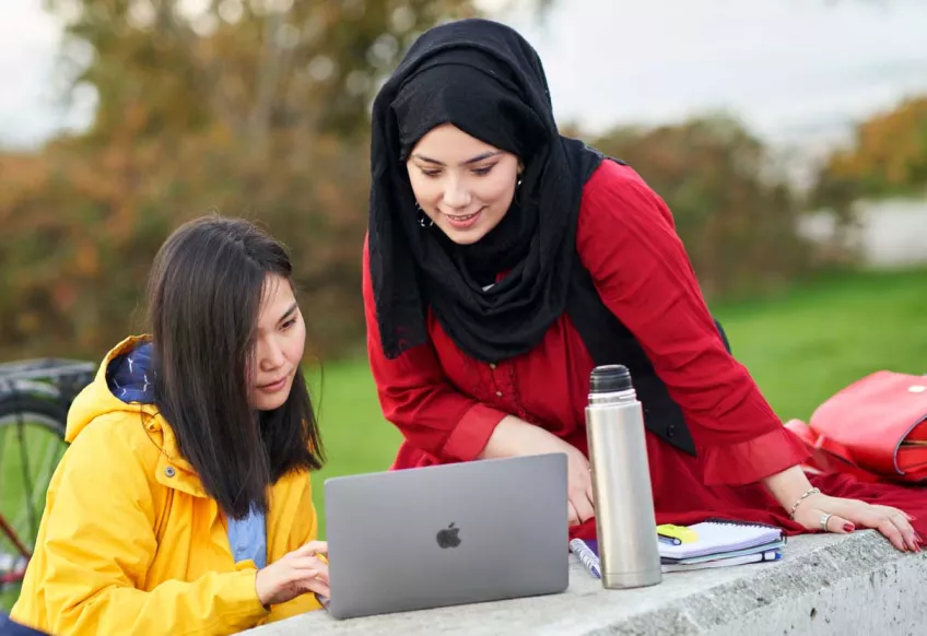 Two students sitting outside looking at computer. Photo.